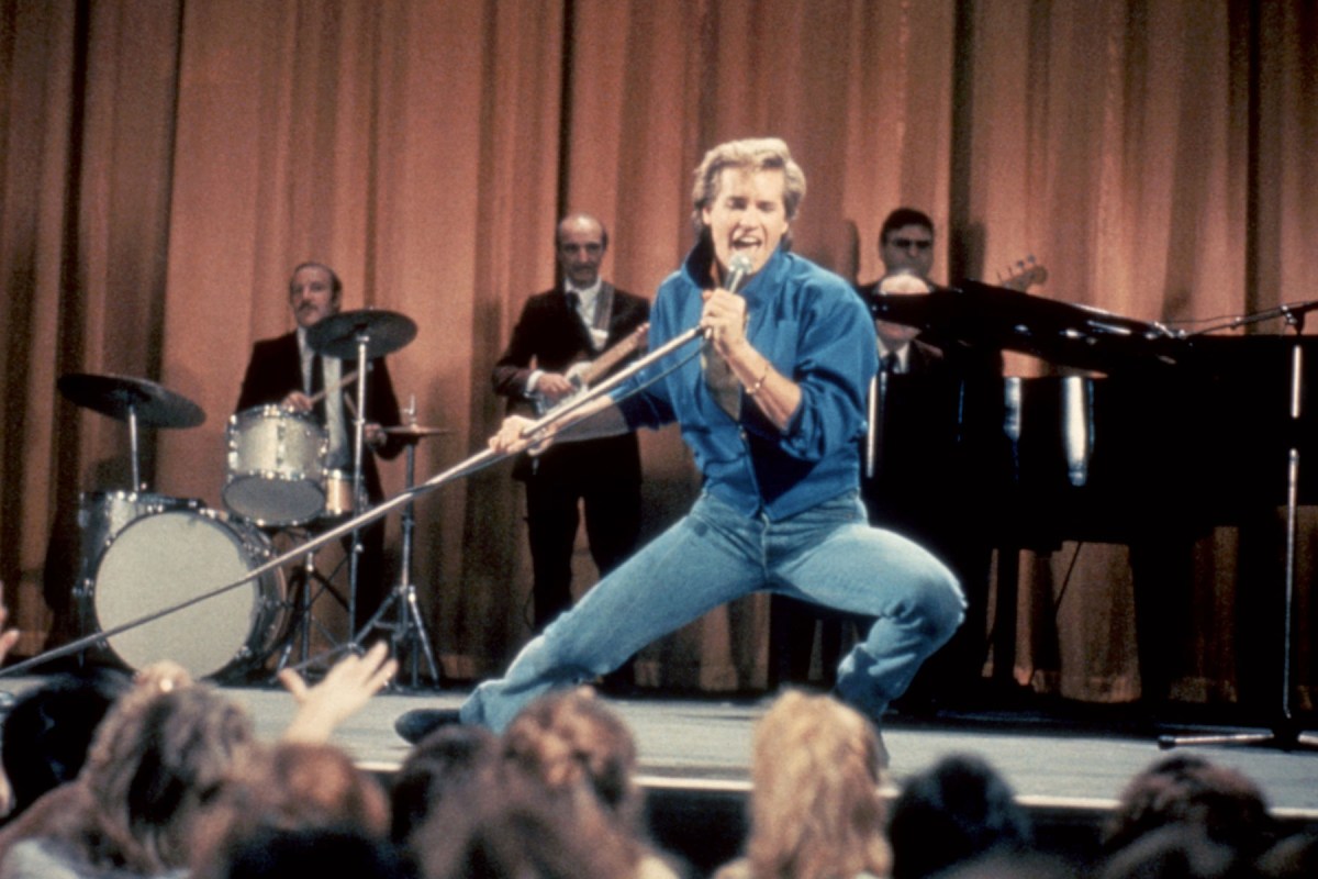 Nick Rivers singing into a microphone onstage, with his band behind him